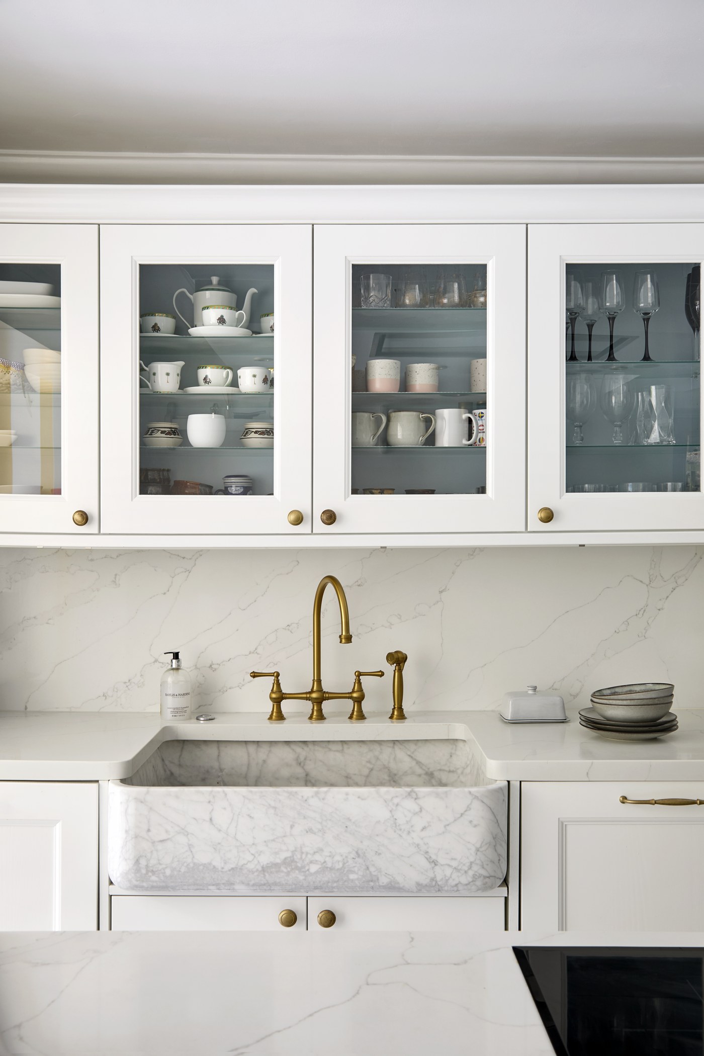 Marble kitchen detail at Achilles Road: glazed wall cabinets, brass bridge tap and stone sink surround