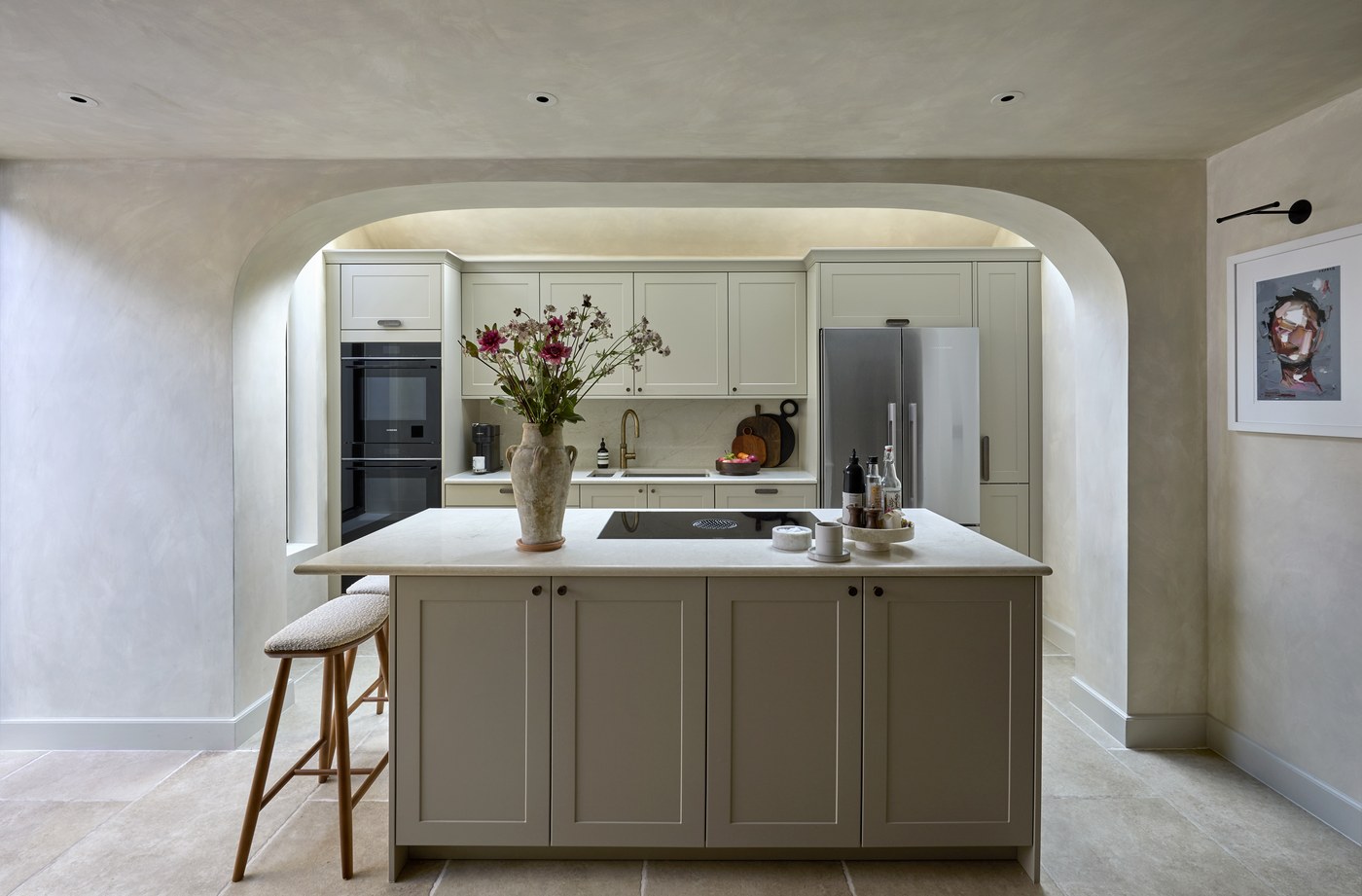 Honeywell Road SW11 — kitchen framed by a broad limewashed arch, with painted cabinetry, a stone-topped island and concealed lighting washing the vaulted ceiling