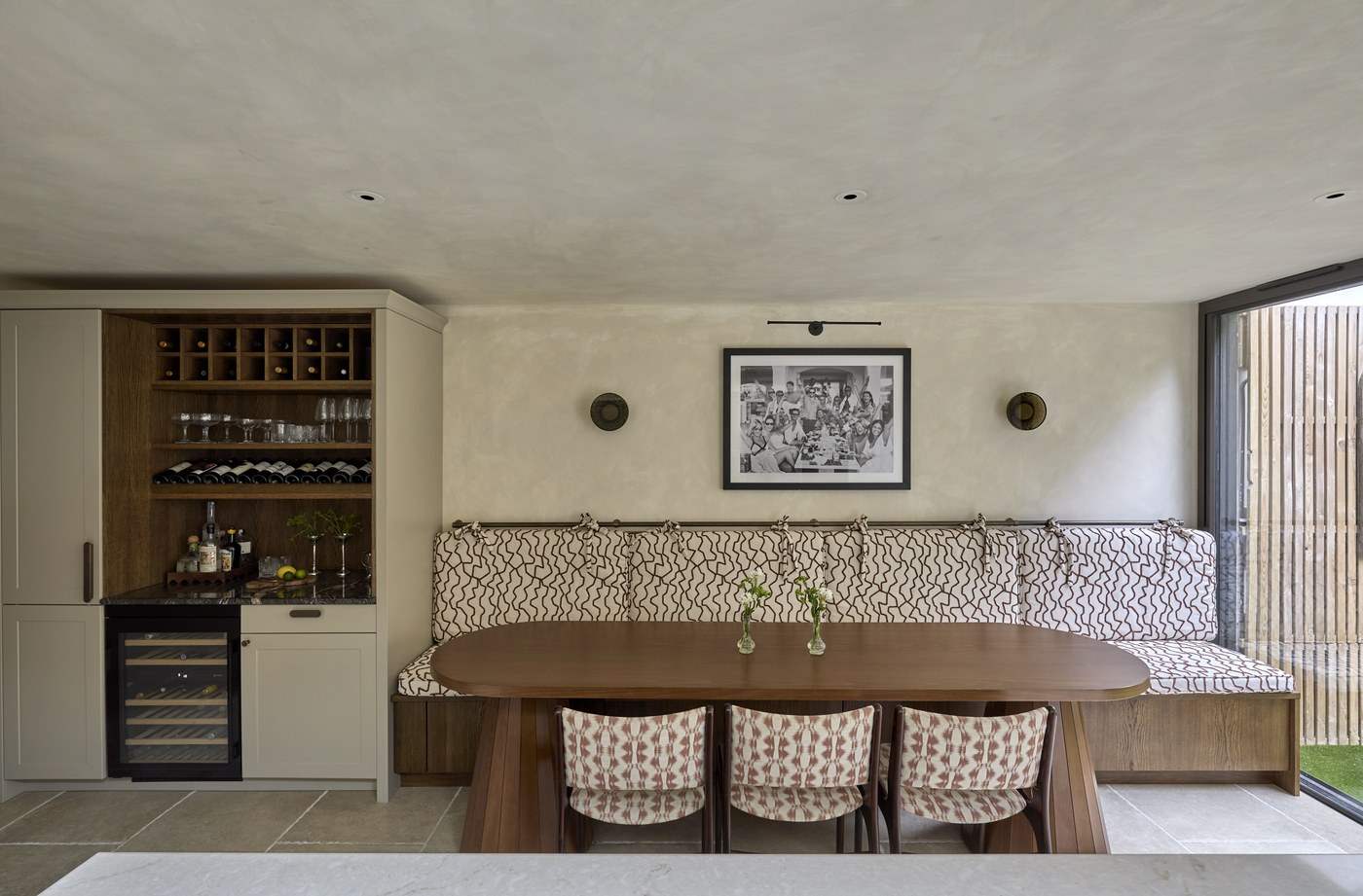 Honeywell Road SW11 — dining area with a fitted upholstered banquette against a limewashed wall, stone floor and a drinks cabinet in painted and oak joinery