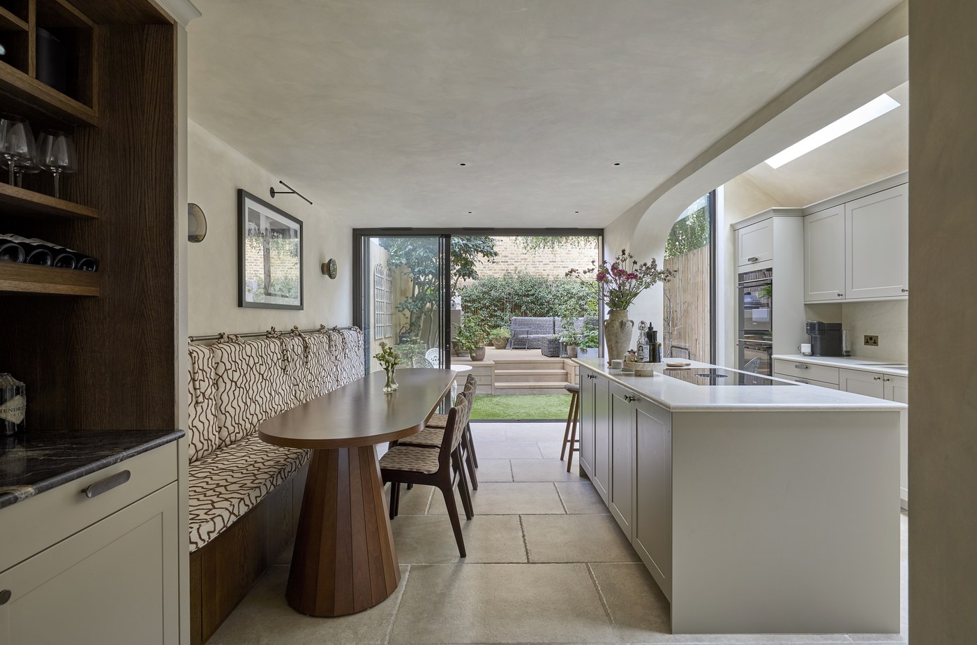 Honeywell Road SW11 — the length of the new kitchen and dining room to the garden, with a fitted banquette, stone floor, curved limewash wall and a rooflight over the kitchen