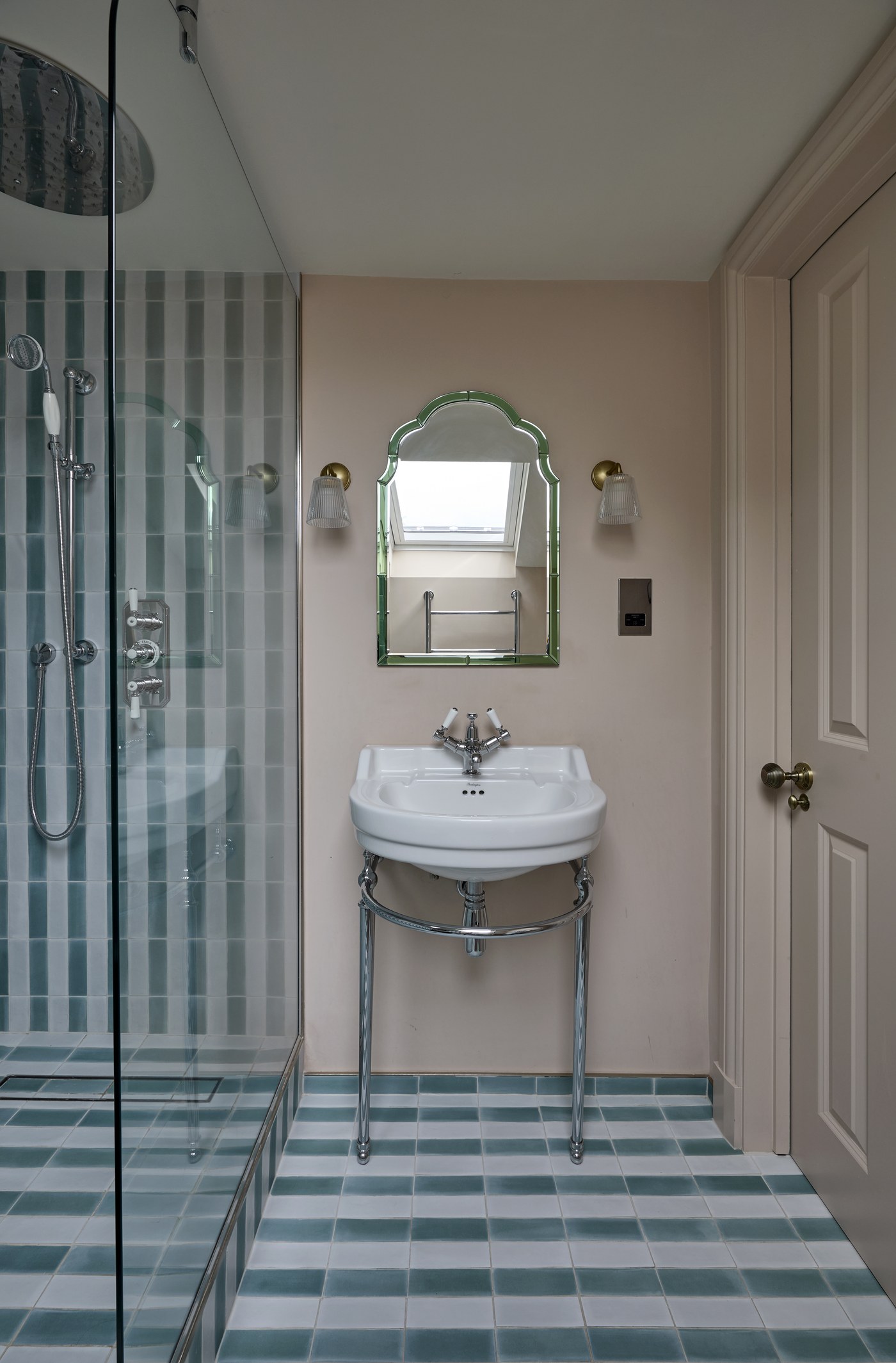 Shower room at Melrose Gardens lined in striped tiling, with an arched mirror and console basin